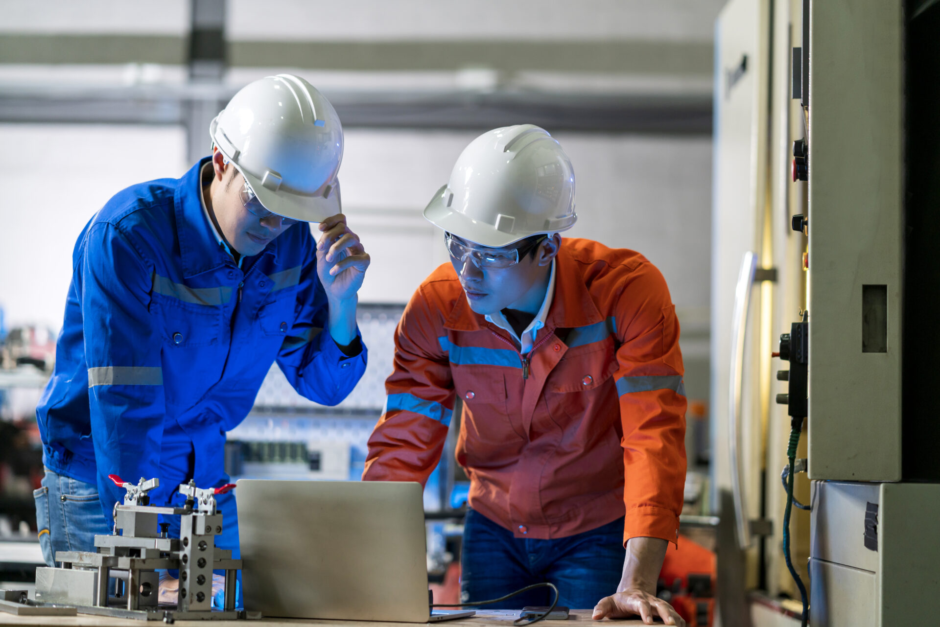 Male Asian engineer professional having a discussion standing concult cnc machine in the factory ,two asian coworker brainstorm explaining and solves the process of the cnc operate machine